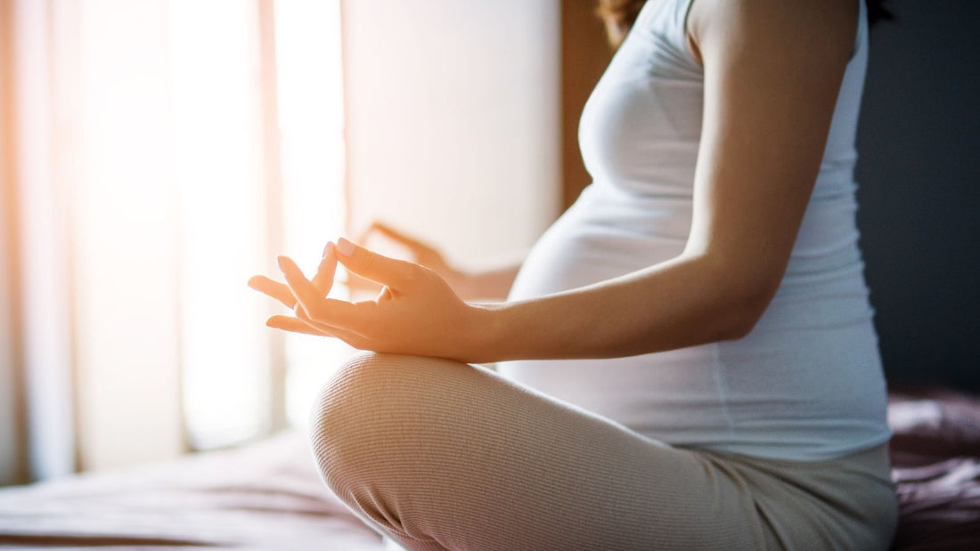 Un femme enceinte assise sur un lit faisant une position de yoga.