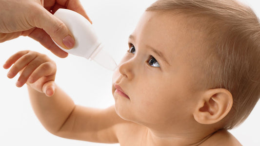 Un bébé de face avec un mouché bébé poire à l'entrée de la narine.