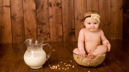 Un bébé dans un saladier de céréale à côté d'un pichet de lait infantile