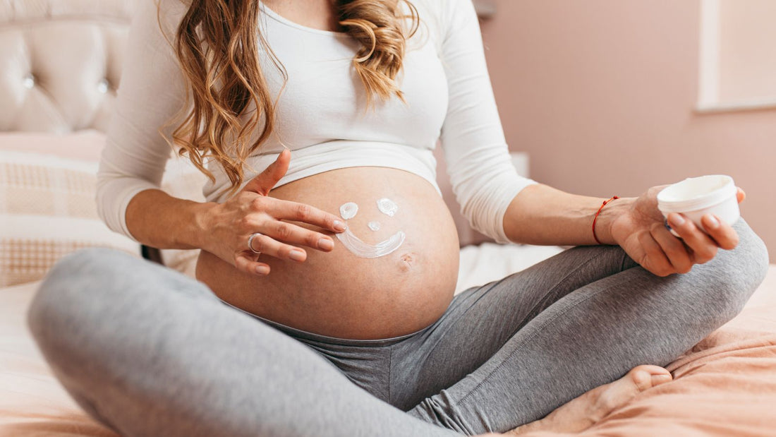 Une femme enceinte assise en tailleur avec un bonhomme qui sourit dessiné en crème sur le ventre.