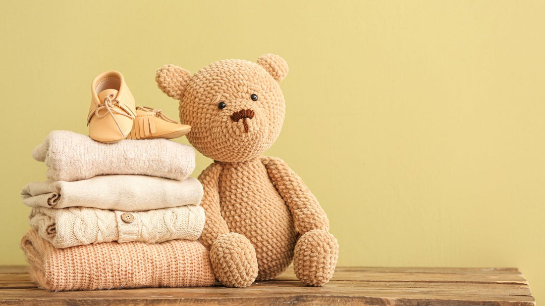 Une pile de vêtement de bébé avec une peluche ourson contre