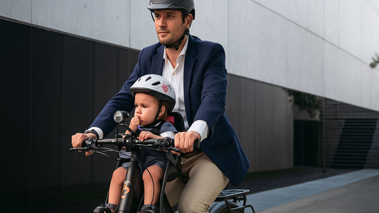 Un papa avec son enfant en vélo, le porte bébé devant.