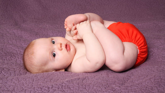 Un bébé en couche lavable allongé sur une couverture violette les pies dans ses mains.