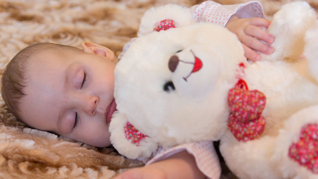 Un bébé endormi avec sa peluche dans les bras.