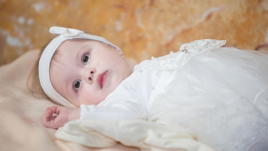 Un bébé habillé d'une robe blanche allongé sur un lit