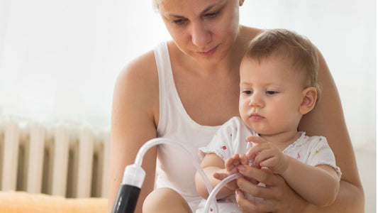 Un bébé assis sur les genoux de sa maman qui lui nettoie le nez avec un mouche bébé